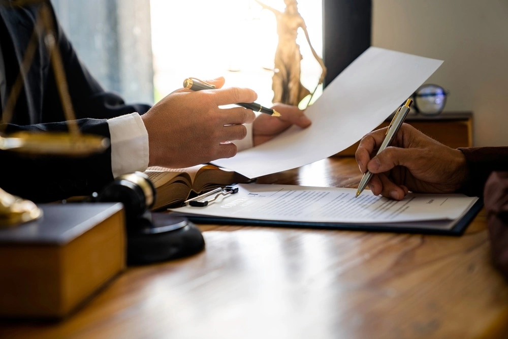 A person signs legal documents with a lawyer, representing the legal process for obtaining guardianship or power of attorney.