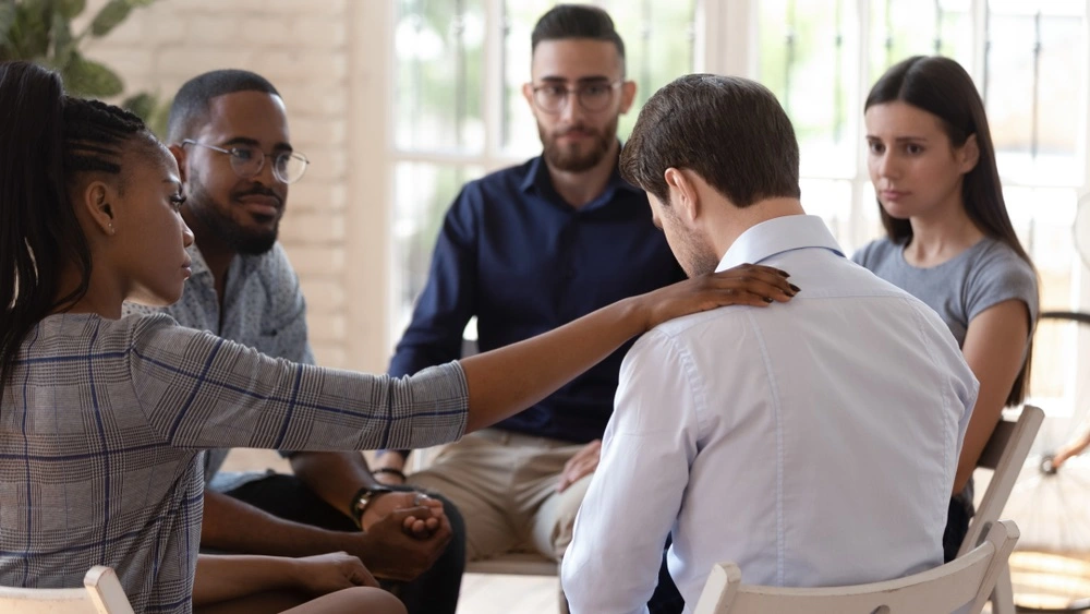 A person surrounded by a supportive group in counseling, representing the treatment and aftercare phases of recovery.