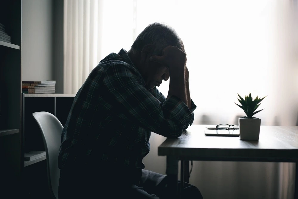 A distressed person sits in a dark room, symbolizing the need for intervention and the initial identification process for initiating the Marchman Act.